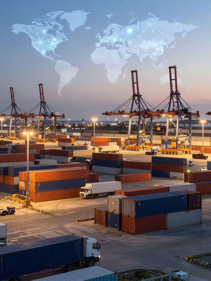 Container port at dusk with global trade routes overlaid, cranes and trucks moving cargo.
